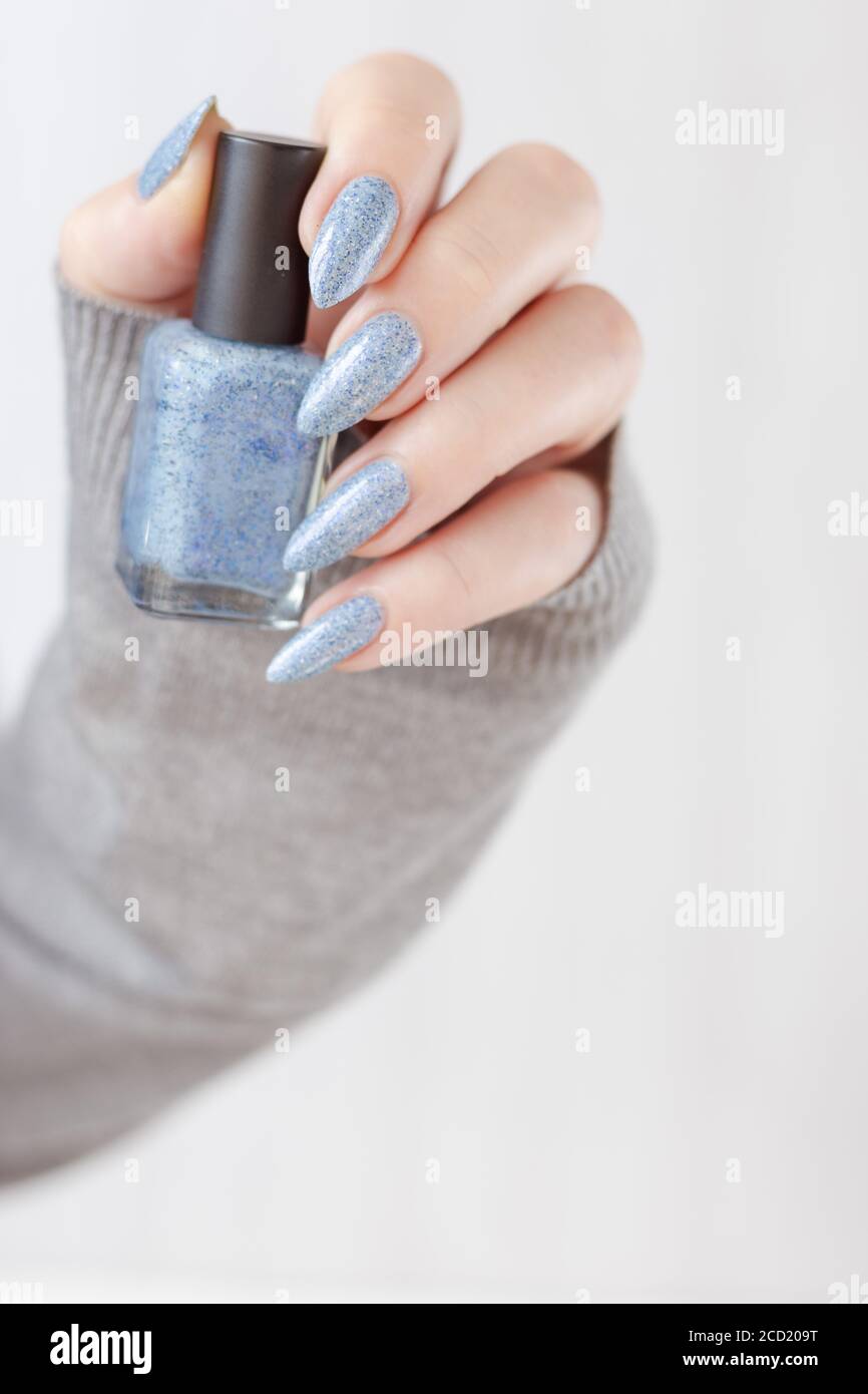 Female hand with long nails and light blue manicure with bottles of nail  polish Stock Photo - Alamy
