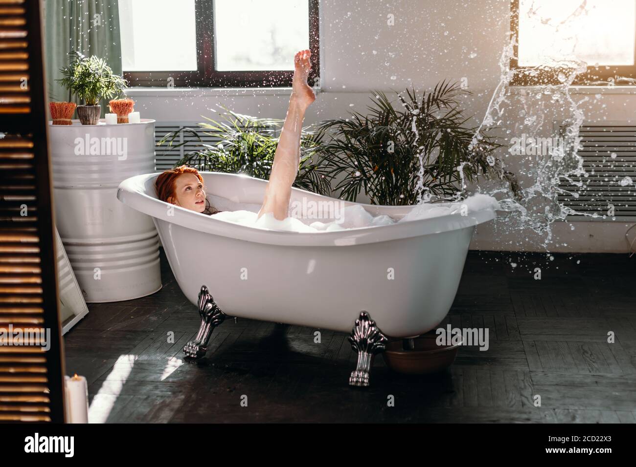 Relaxing woman having fun raises her slim legs in air while taking foam