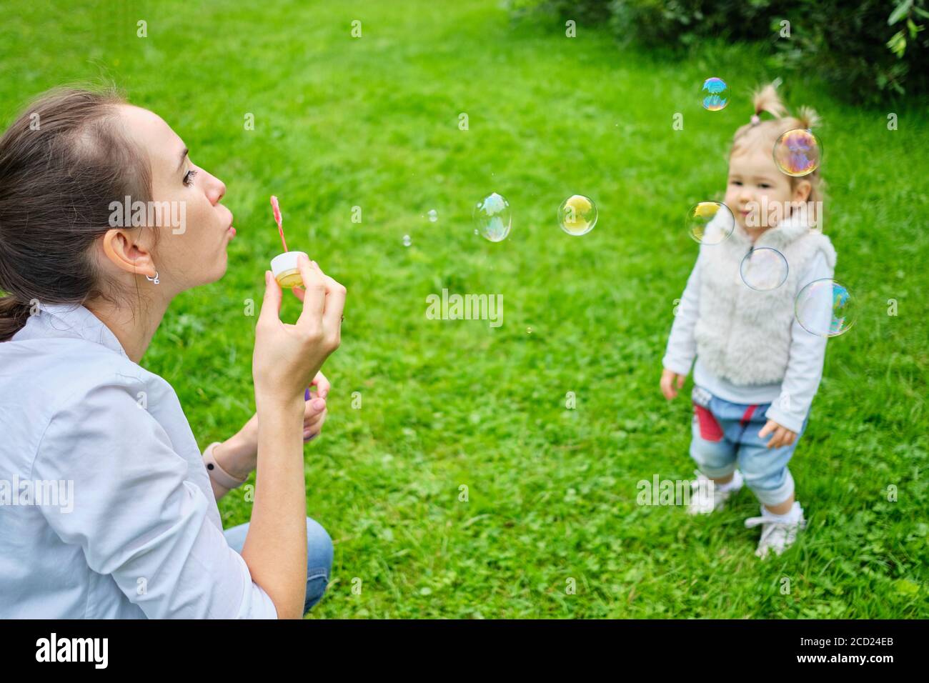 Portrait of happy caucasian child running in the park with mom and blow bubbles. Stock Photo