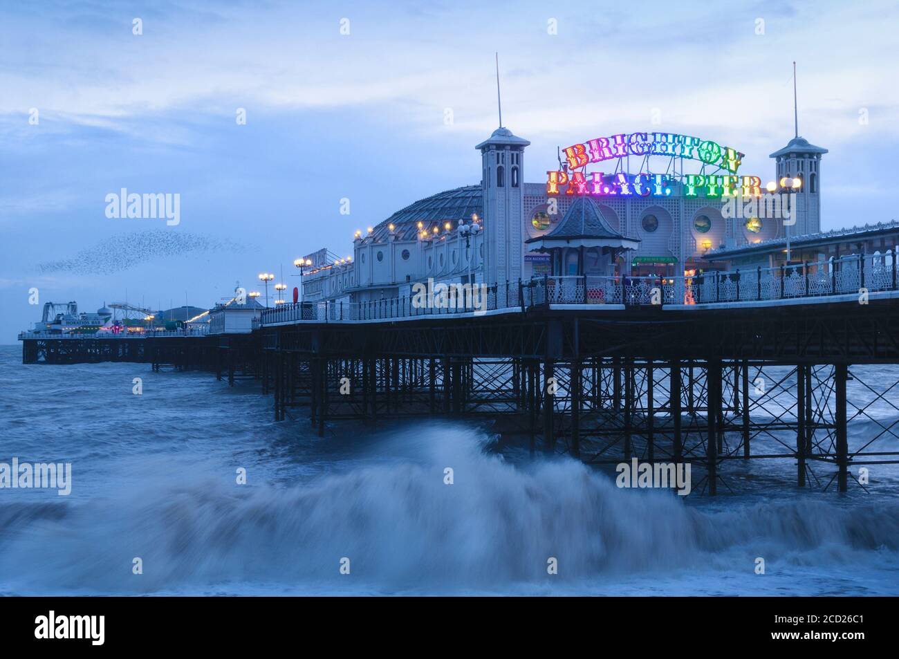 Brighton Palace Pier at dusk with colourful neon lights and a mumuration of starlings in the background, Brighton and Hove, East Sussex, England, UK Stock Photo