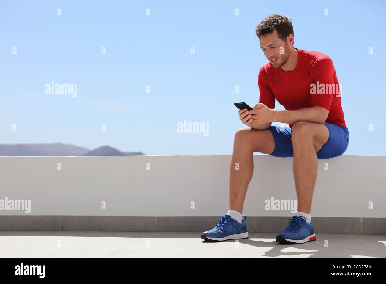 Athlete man watching video on phone screen at home or outdoor gym. Technology and sports athlete holding cellphone. Happy fit young adult in Stock Photo