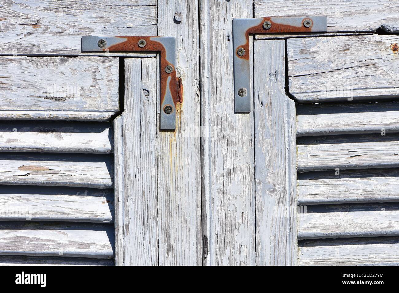 Weathered wooden window shutters with white paint peeling off and rusty