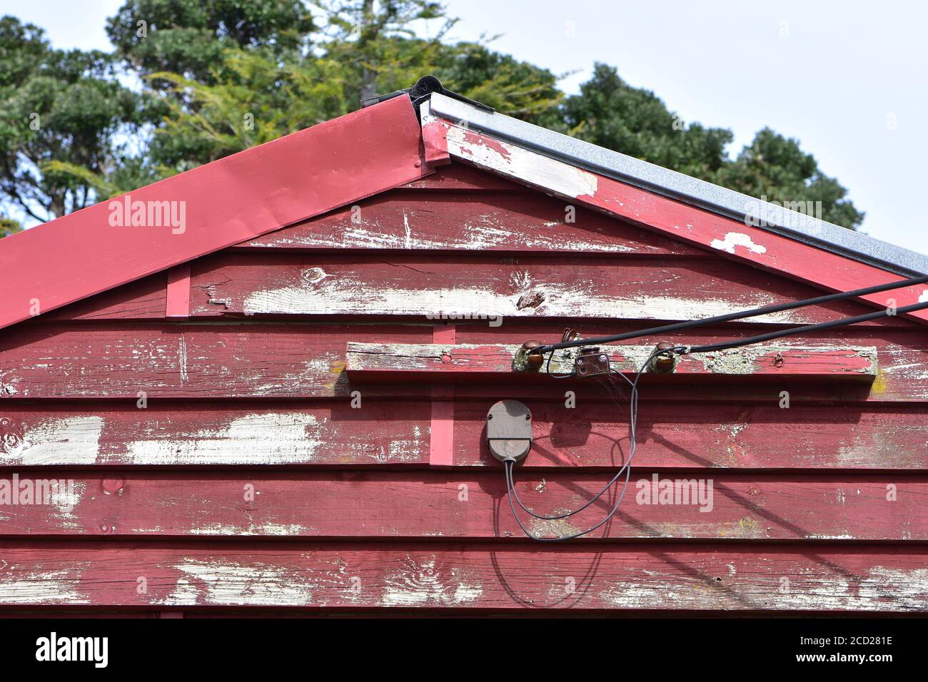 Electric wires connecting weathered wooden shed painted red to power