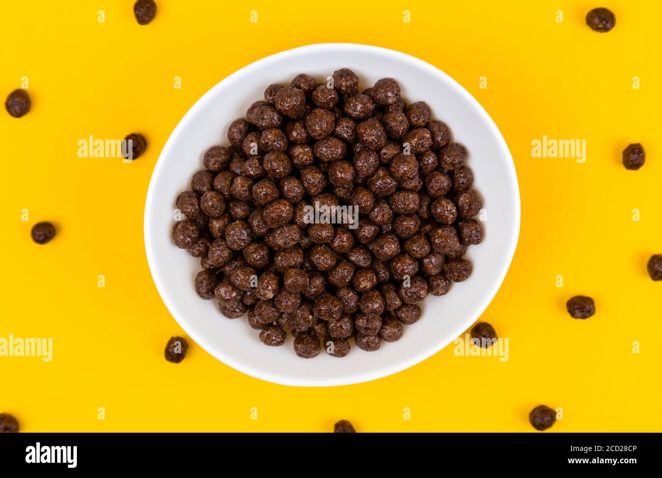 White bowl with chocolate corn cereal balls and milk on yellow background, top-down view. Modern fresh breakfast image. Stock Photo