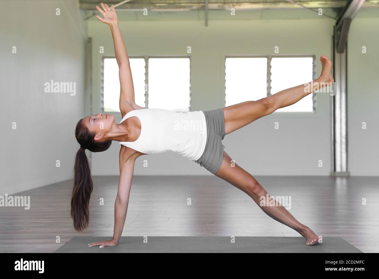 Yoga woman planking doing side plank leg lift core exercises in yoga class at fitness gym. Stock Photo