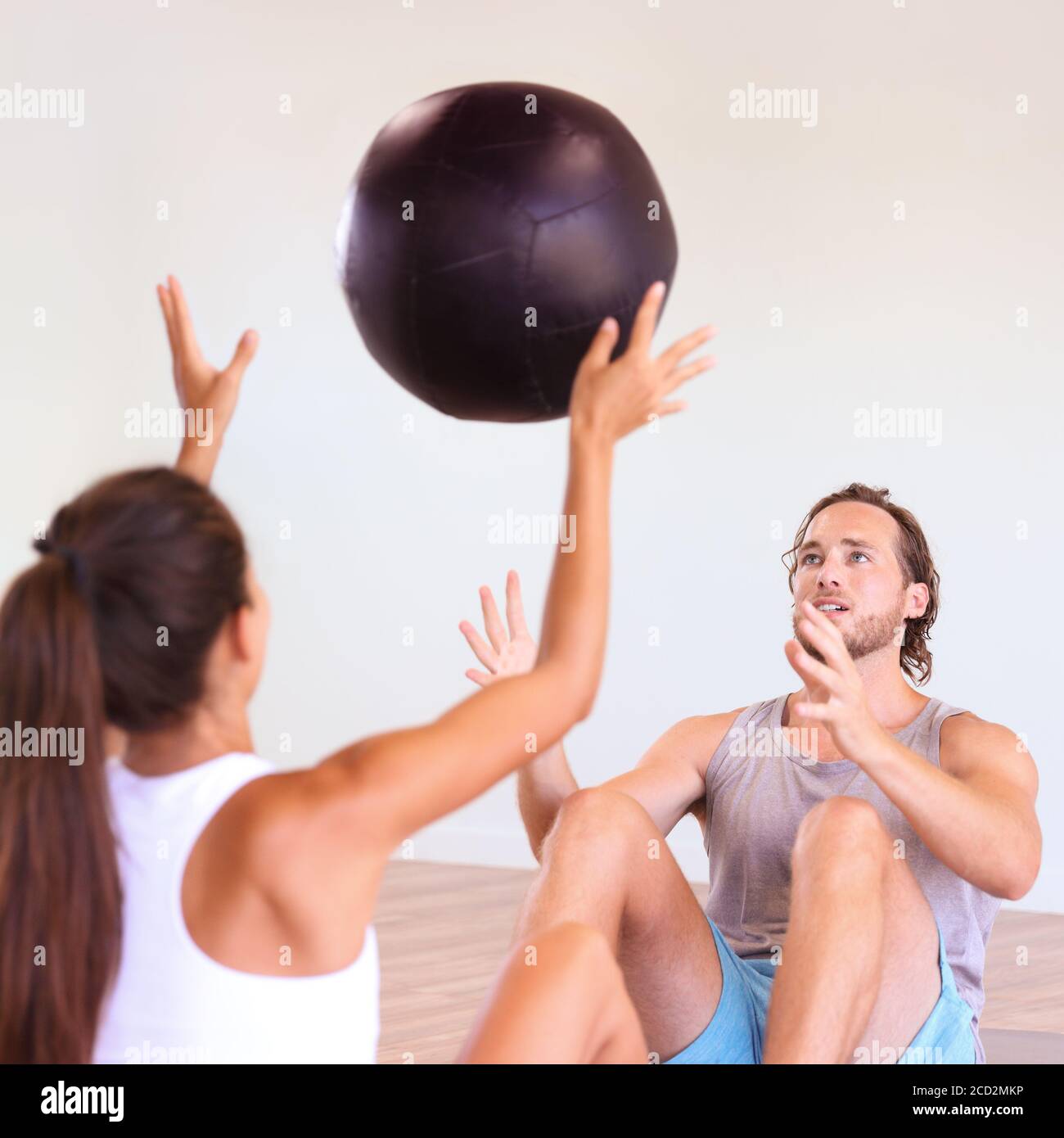 Couple training together at gym. Cross training class at fitness centre, two friends working out throwing medicine ball at each other, sports buddy. Stock Photo