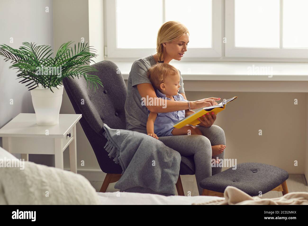 Mother and child Toddler reads a story in a book in a room with a window. Mothers Day. Stock Photo