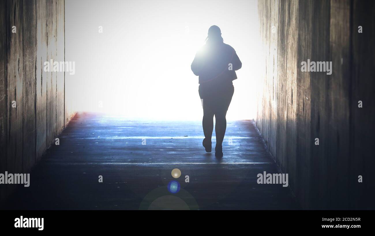 A lone isolated figure fading away heading or walking towards a bright light at the end of tunnel. Grief, death, dying suicide, faith concept. Crossin Stock Photo