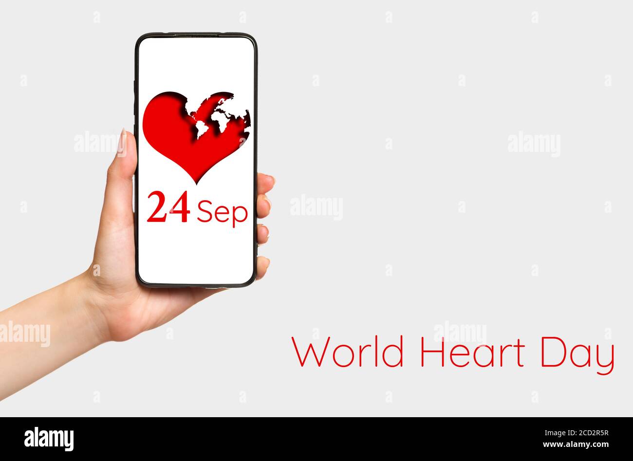 A females hand holds a smartphone with a red heart depicted on it. White background. Copy space. Concept of world heart day, September 24. Stock Photo