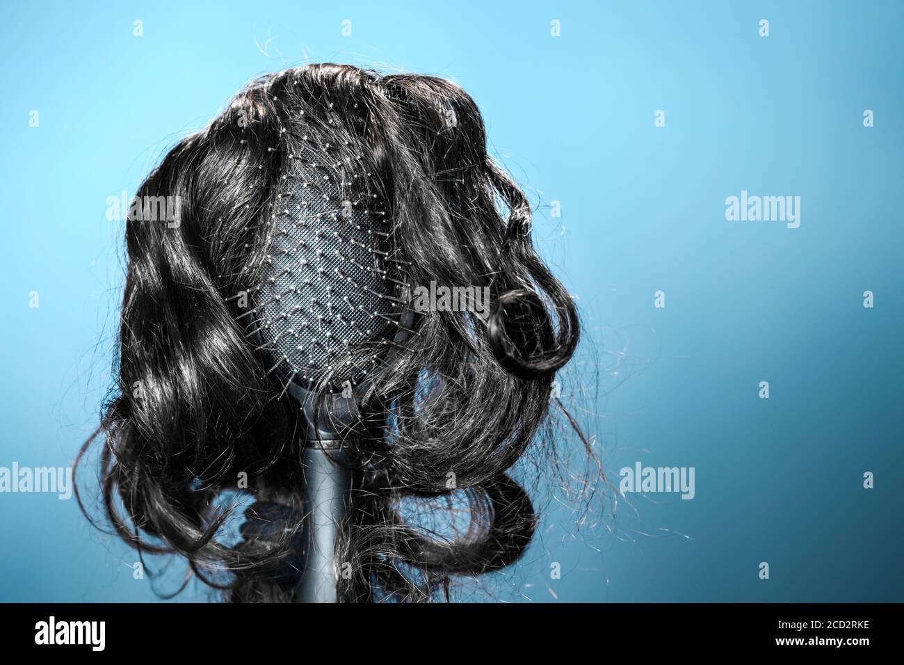 Females hair. Black hairbrush with a black wig, looks like a woman's head with a hairstyle. Blue background. Copy space. Concept of beauty salon, hair Stock Photo