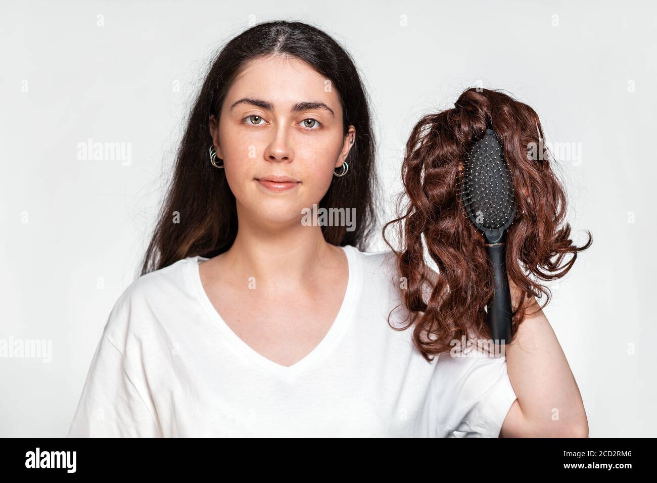 Portrait of a pretty woman holds a comb with a wig on it. White background. Concept of hair care and hair loss. Stock Photo