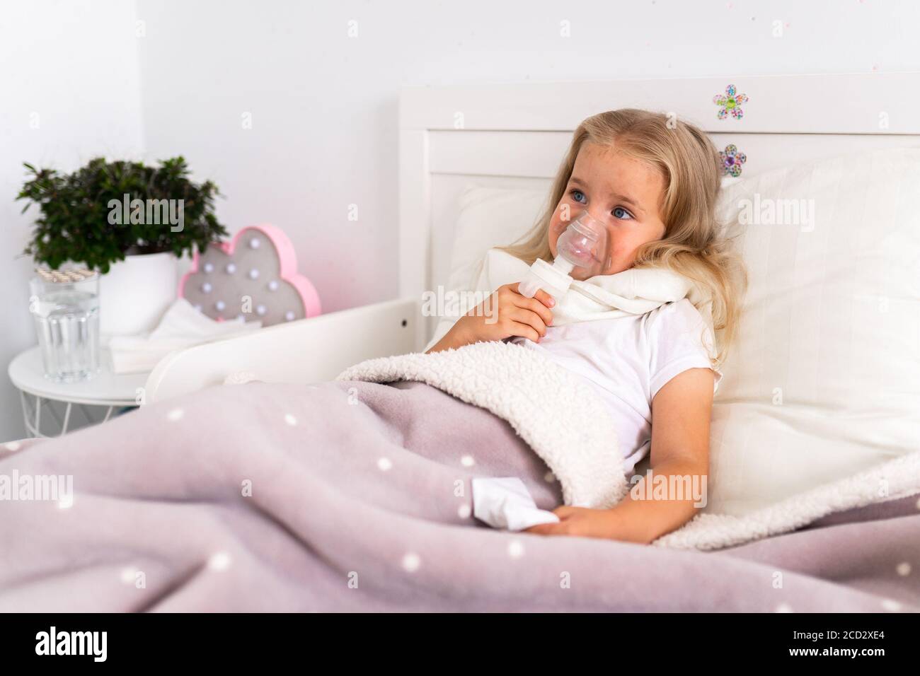 Little girl makes inhalation with a nebulizer in the house lying in bed