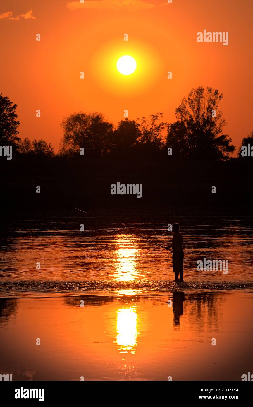 Fisherman fishing at sunset, sun reflecting in water Stock Photo - Alamy