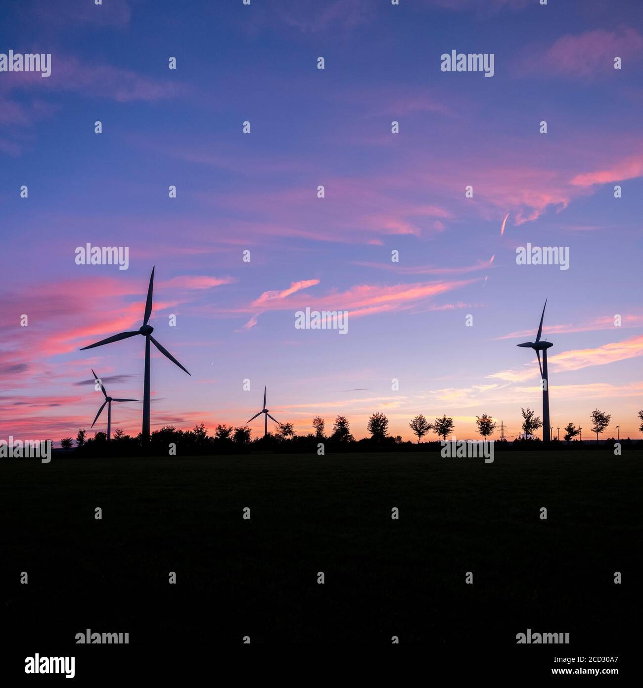 wind turbines and trees form silhouettes against colorful sunset Stock ...