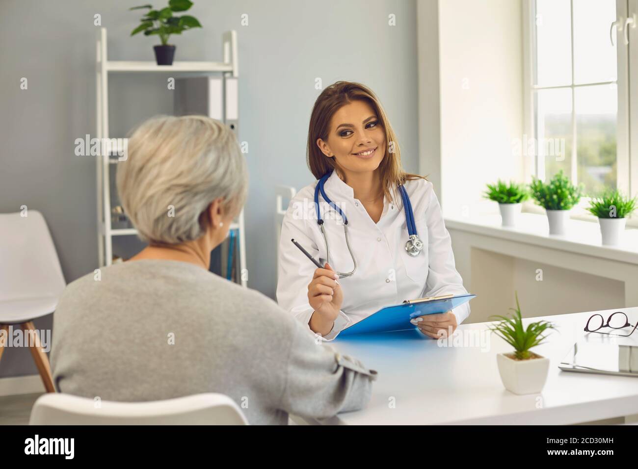 Smiling woman doctor therapist consulting senior woman patient in medical clinic office Stock Photo