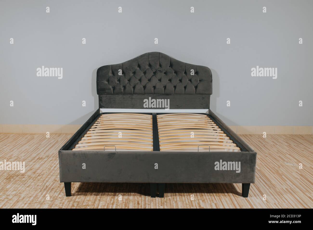 Bed with gray upholstery and without mattress in an empty room Stock