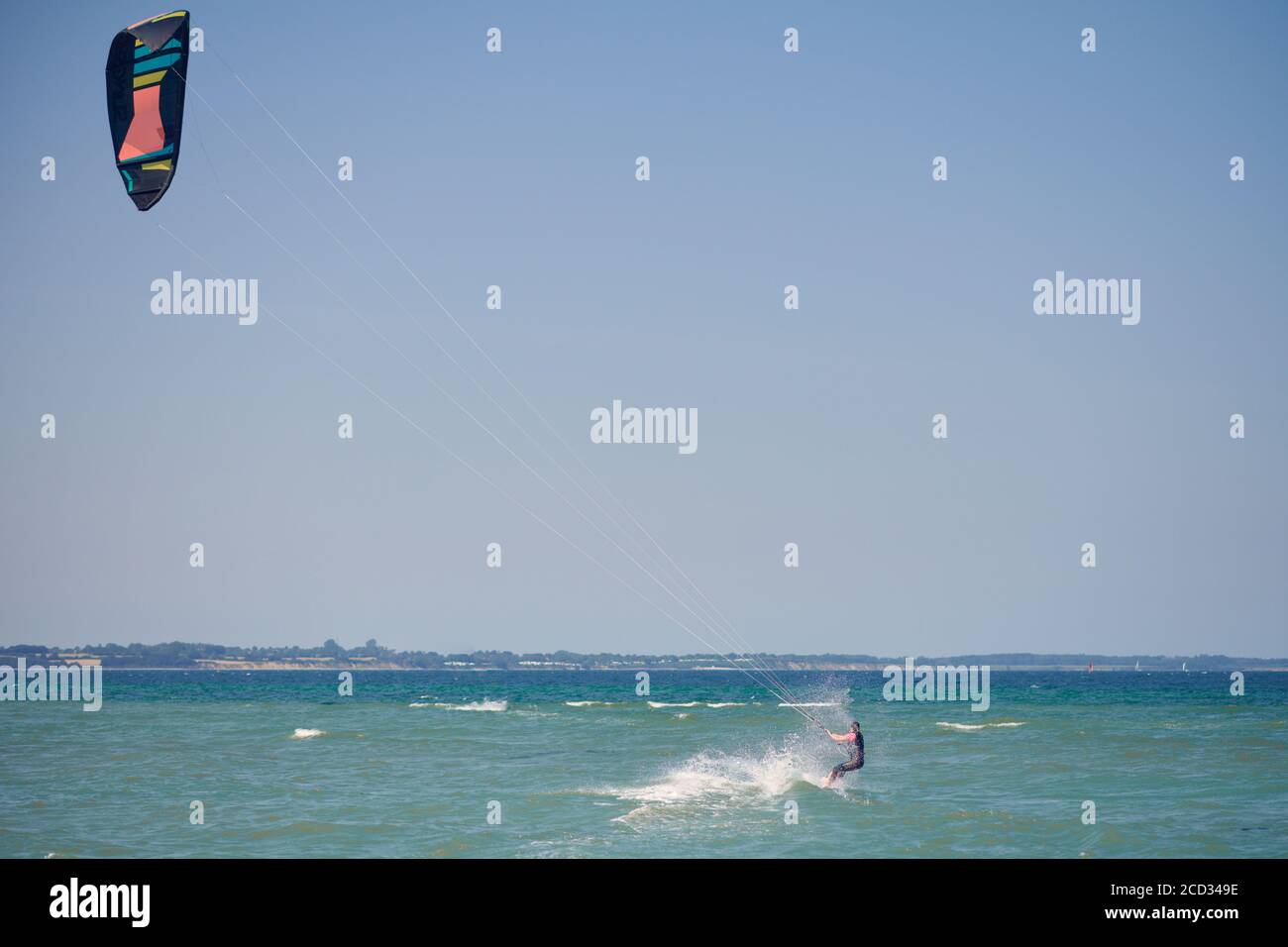 Brunette woman kitesurfing or kite boarding pulling away from the sandy beach making for deeper water on a sunny summer day in a rear view to the came Stock Photo