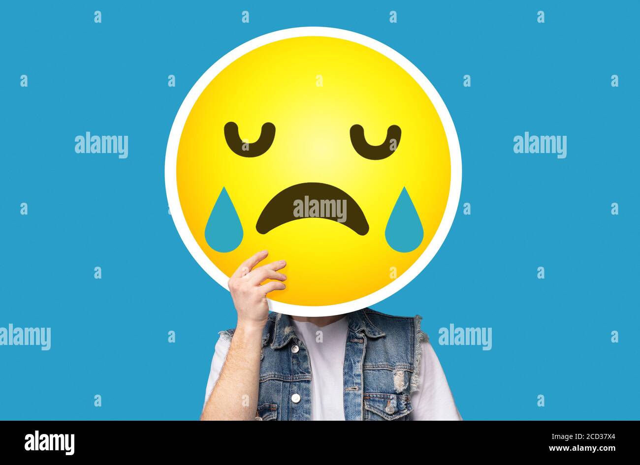 Unrecognizable man hiding his face behind crying sad emoticon emoji Stock Photo