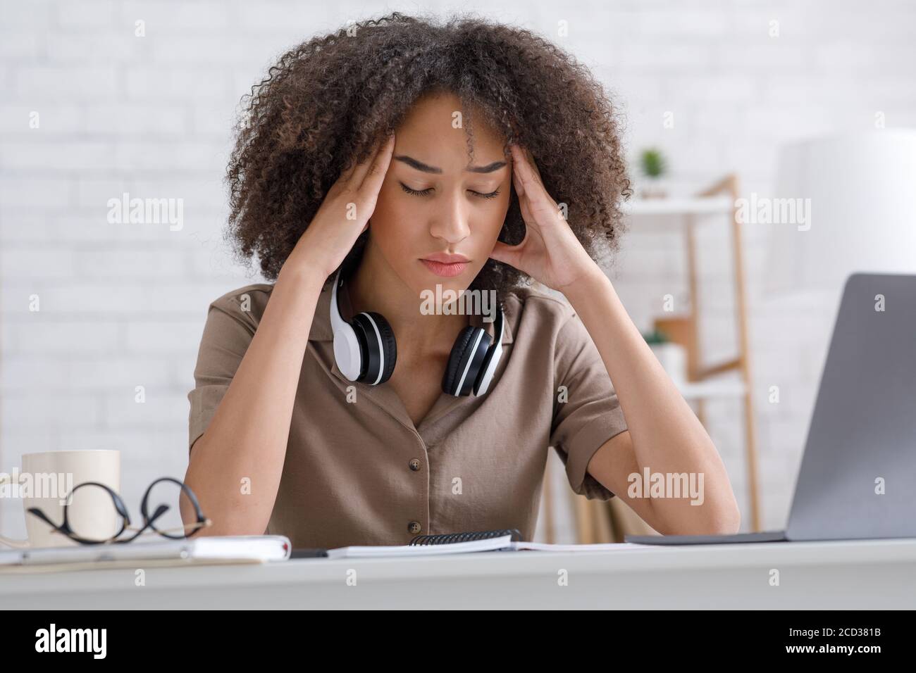 Overwork and big load. Tired business woman with closed eyes, rubs temples in interior of living room Stock Photo