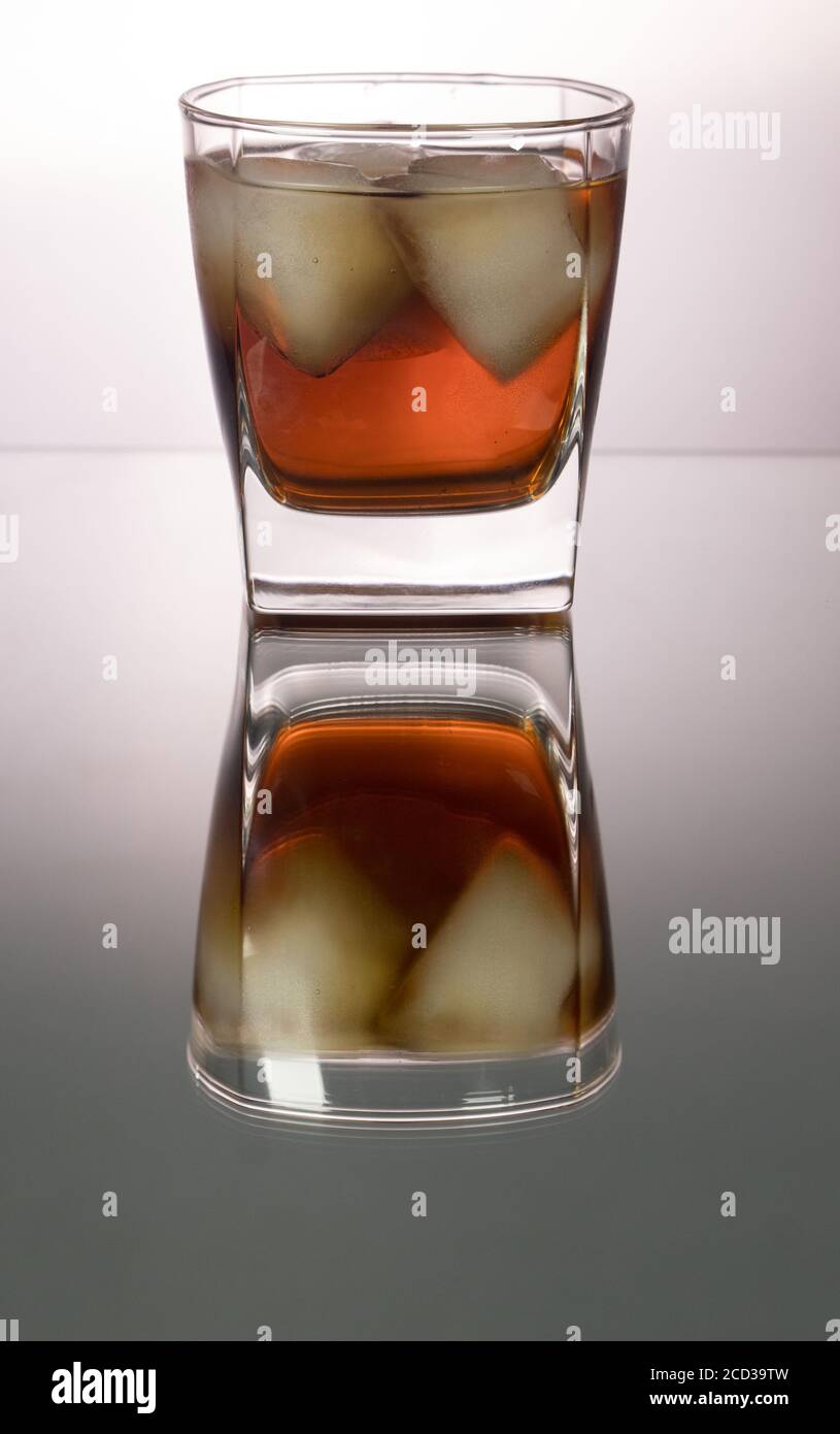 Glass of whiskey with pieces of ice on mirroring table. Vertical image with copy space. Stock Photo