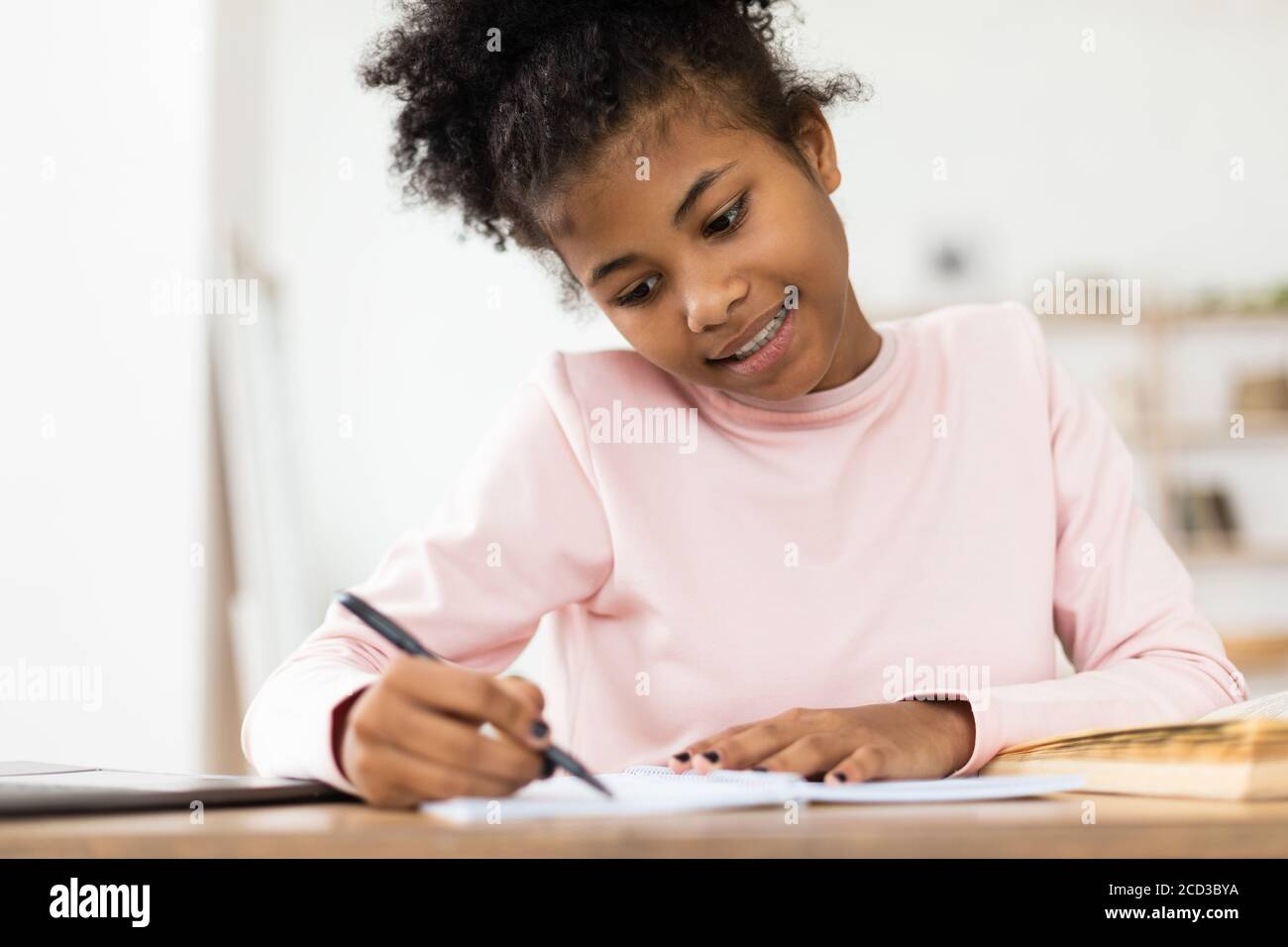 African Teen Girl Doing Homework Writing In Exercise-Book At Home Stock Photo