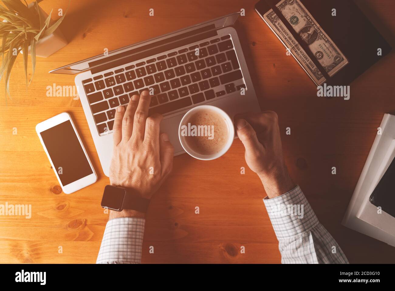 Businessman drinking coffee and typing laptop computer keyboard, overhead shot of office desk in morning Stock Photo