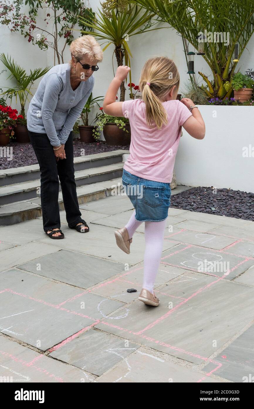 A grandmother teaching her granddaughter a traditional game of hopscotch. Stock Photo