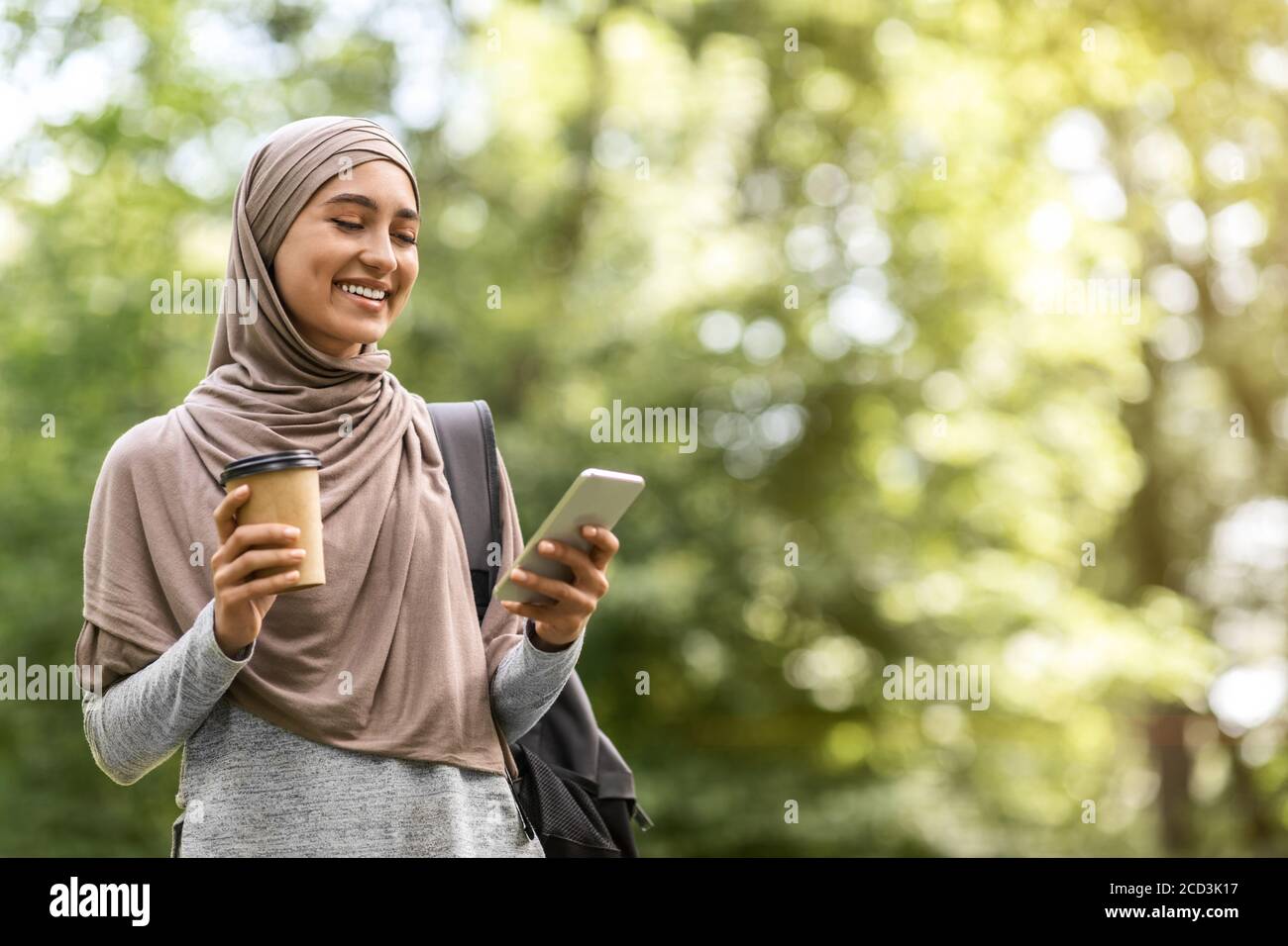 Muslim girl in hijab drinking coffee and using phone Stock Photo