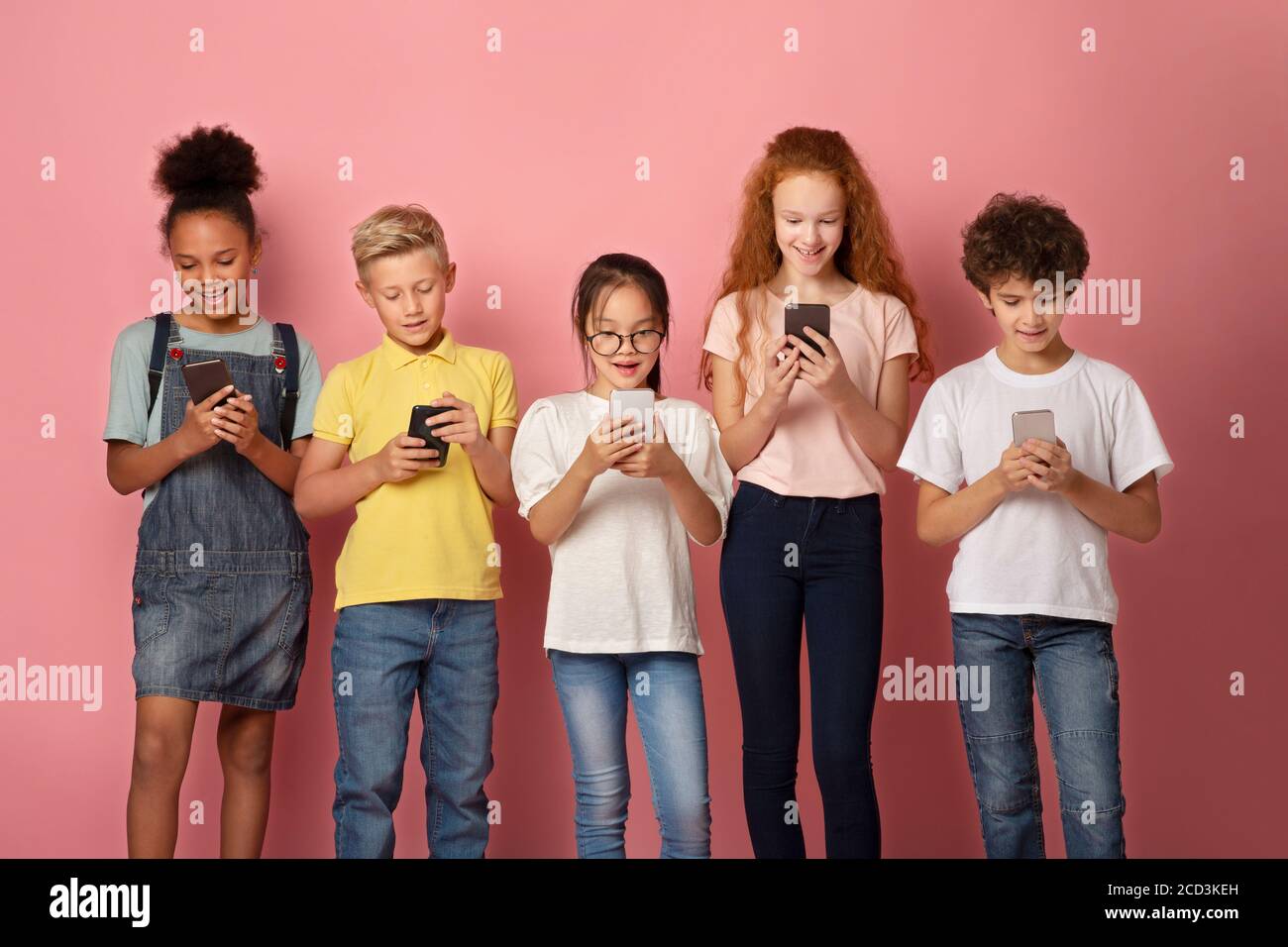 Online education. Adorable multinational schoolkids stuck in smartphones on pink background Stock Photo