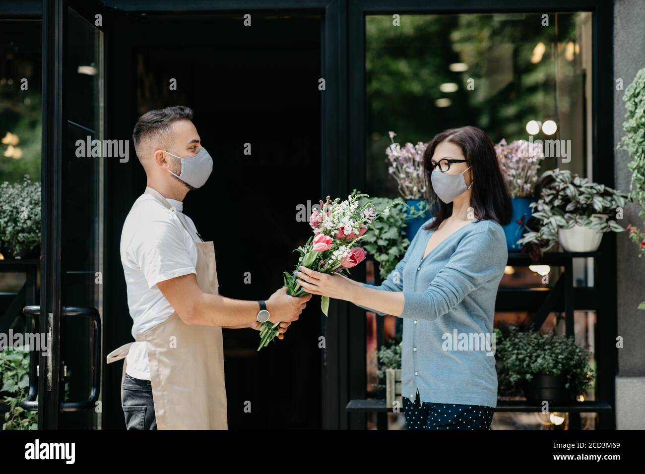 Customer service in flower shop. Man in protective mask gives bouquet to client Stock Photo