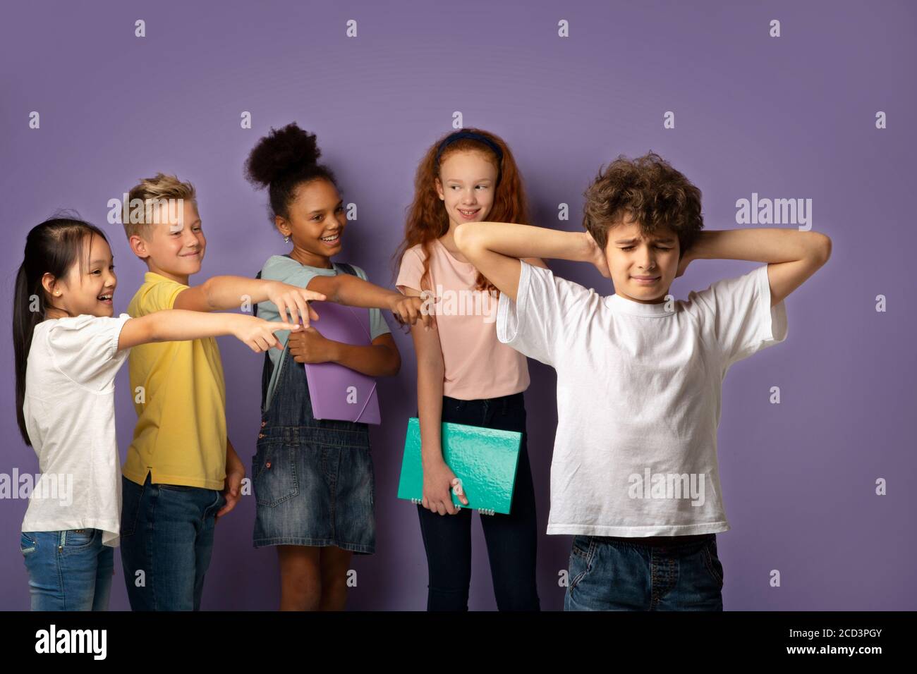 Bullying at schools. Cruel schoolkids harassing unhappy little boy on lilac background Stock Photo