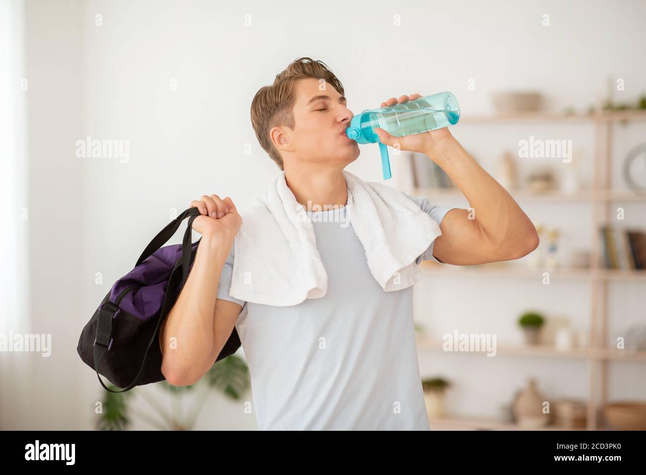Health care and workout. Slender guy drinks water from bottle and holds sports bag Stock Photo