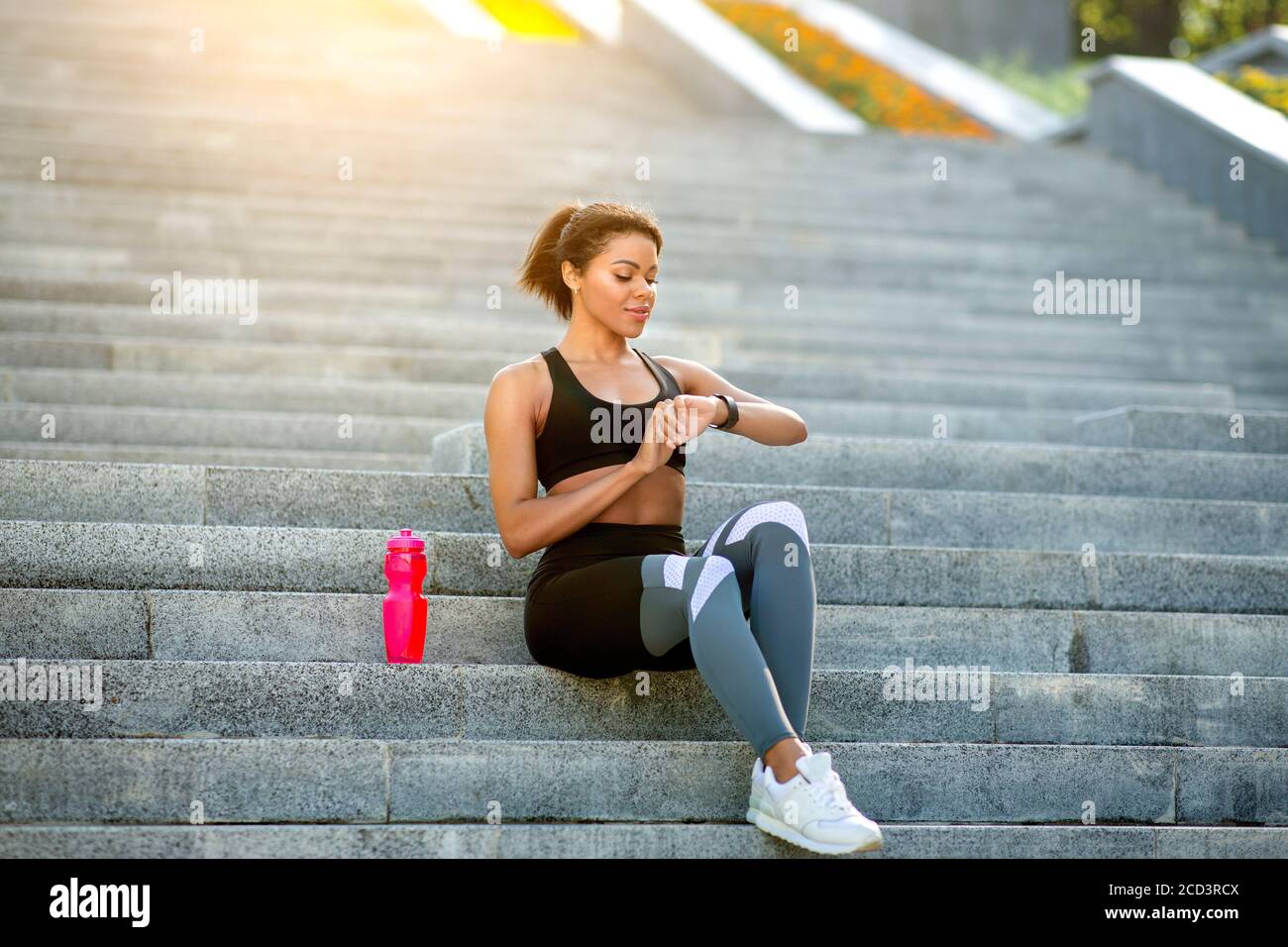 African fitness girl sitting on stairs, checking on smartwatch