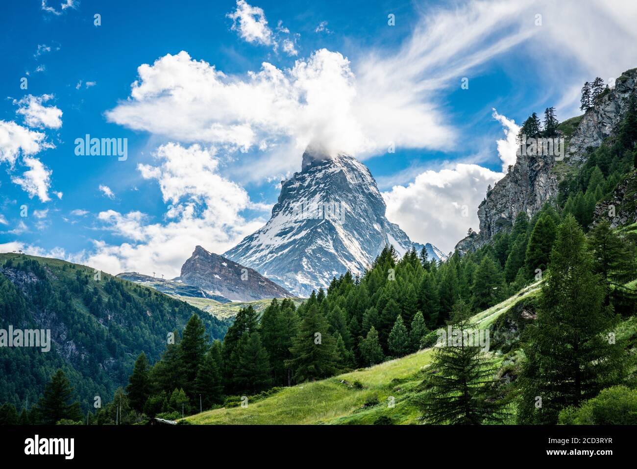 Scenic view of the Matterhorn mountain summit with snow clouds blue sky and green nature during summer in Zermatt Switzerland Stock Photo