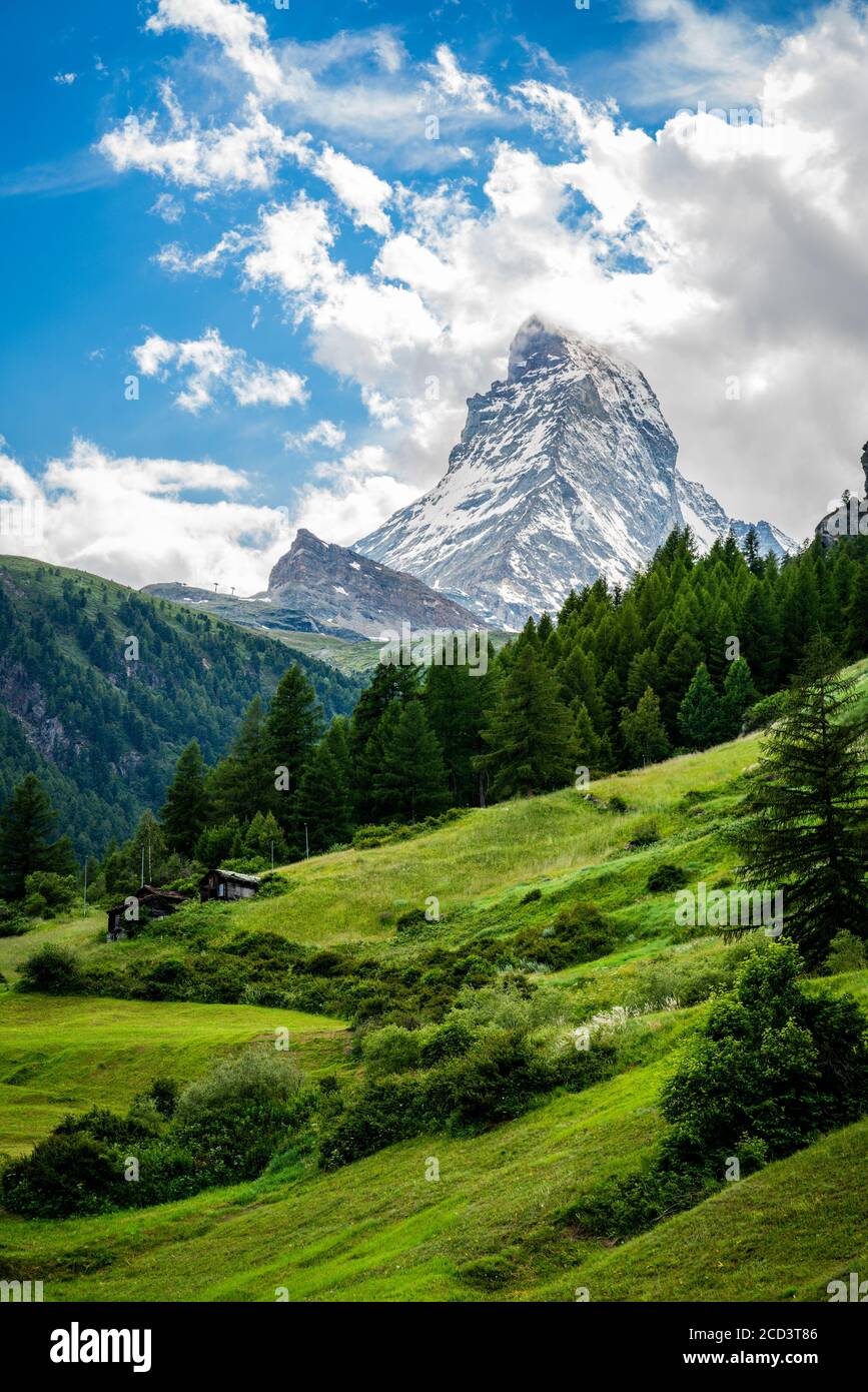 Vertical scenic view of the Matterhorn mountain summit with snow clouds blue sky and green nature during summer in Zermatt Switzerland Stock Photo