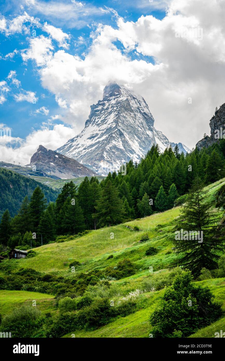 Vertical scenic view of the Matterhorn mountain summit with snow clouds blue sky and green nature during summer in Zermatt Switzerland Stock Photo