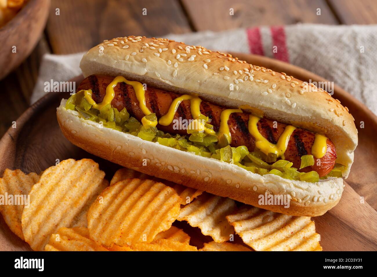 Grilled hot dog with mustard and relish on a sesame seed bun and potato