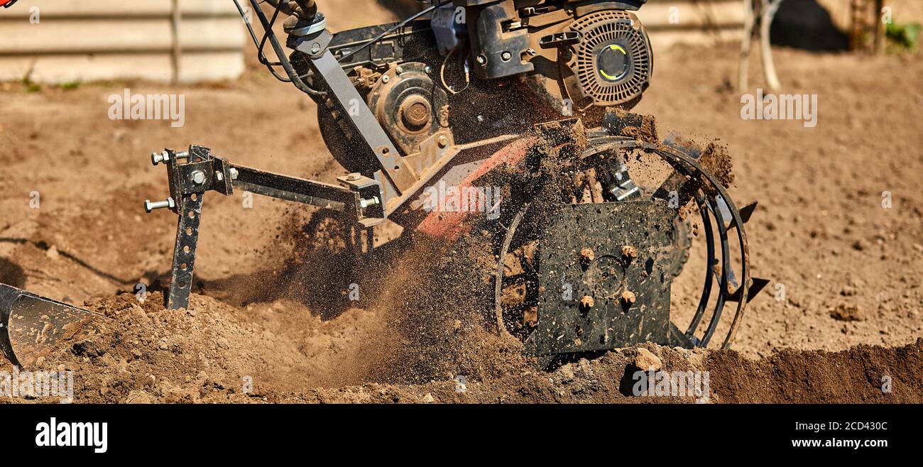 Gardener man cultivate ground soil with tiller tractor or rototiller ...