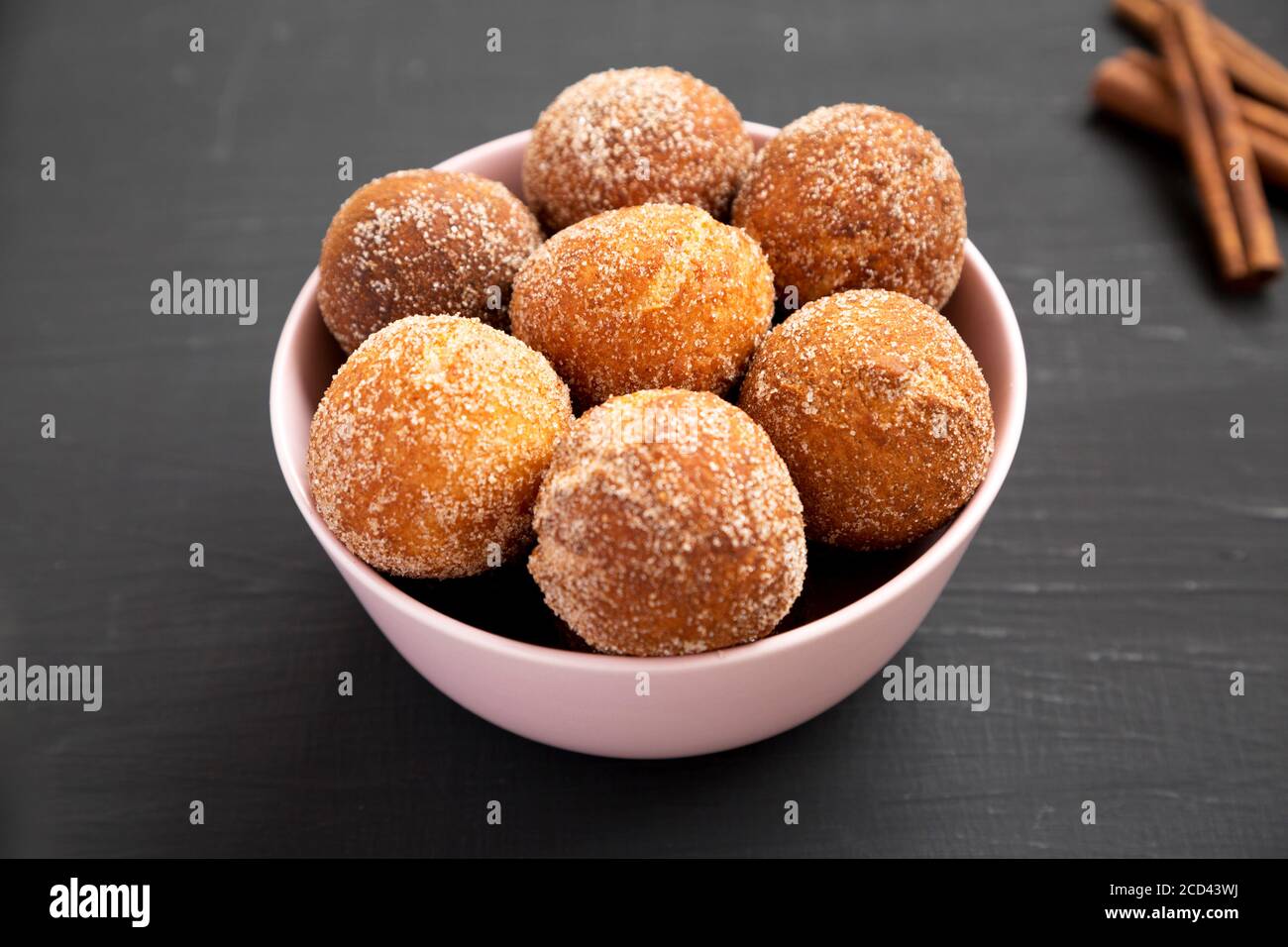 Homemade Fried Donut Holes in a pink bowl on a black surface, side view. Stock Photo