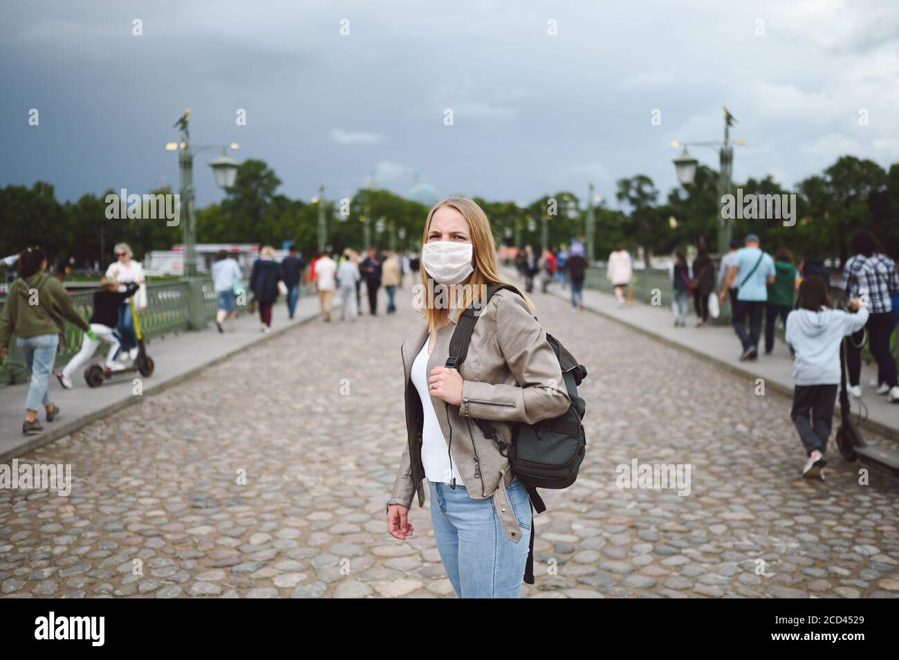 Young blonde woman walking in city street wearing face protective mask ...