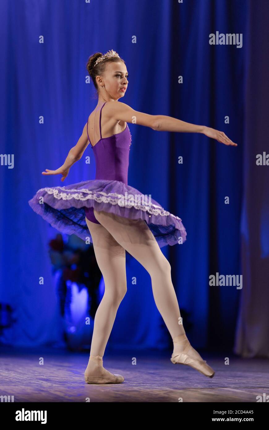 Young girl ballerina in a purple tutu dancing performance on stage in a
