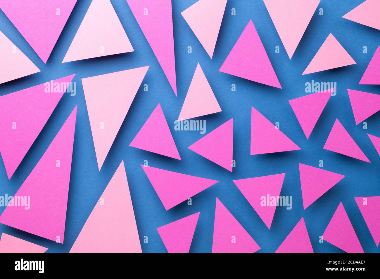 Abstract composition with pink triangular paper shapes over blue background. Top view Stock Photo