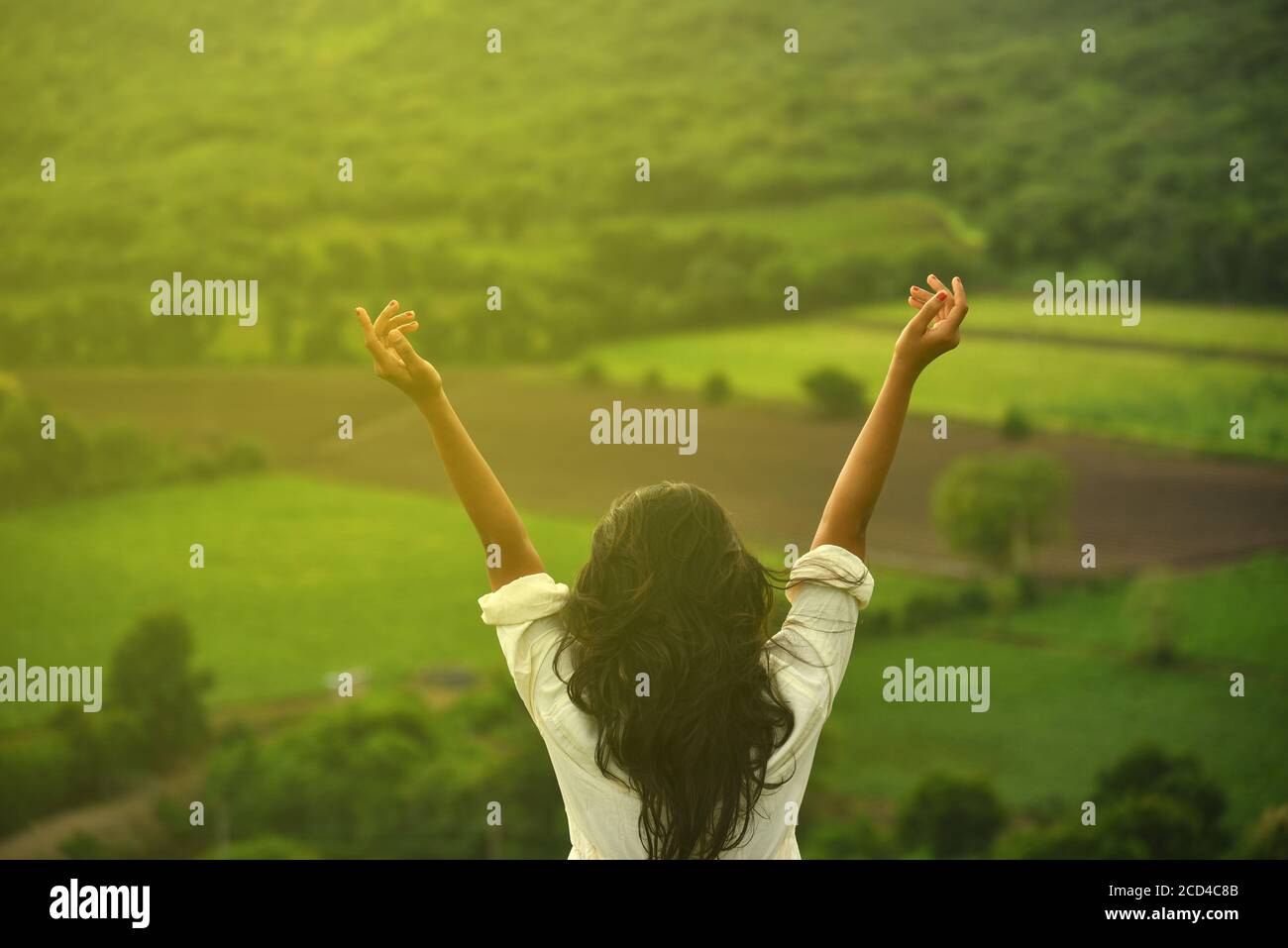 Happy celebrating winning success woman at sunset or sunrise standing elated with arms raised up above her head in celebration of having reached mount Stock Photo