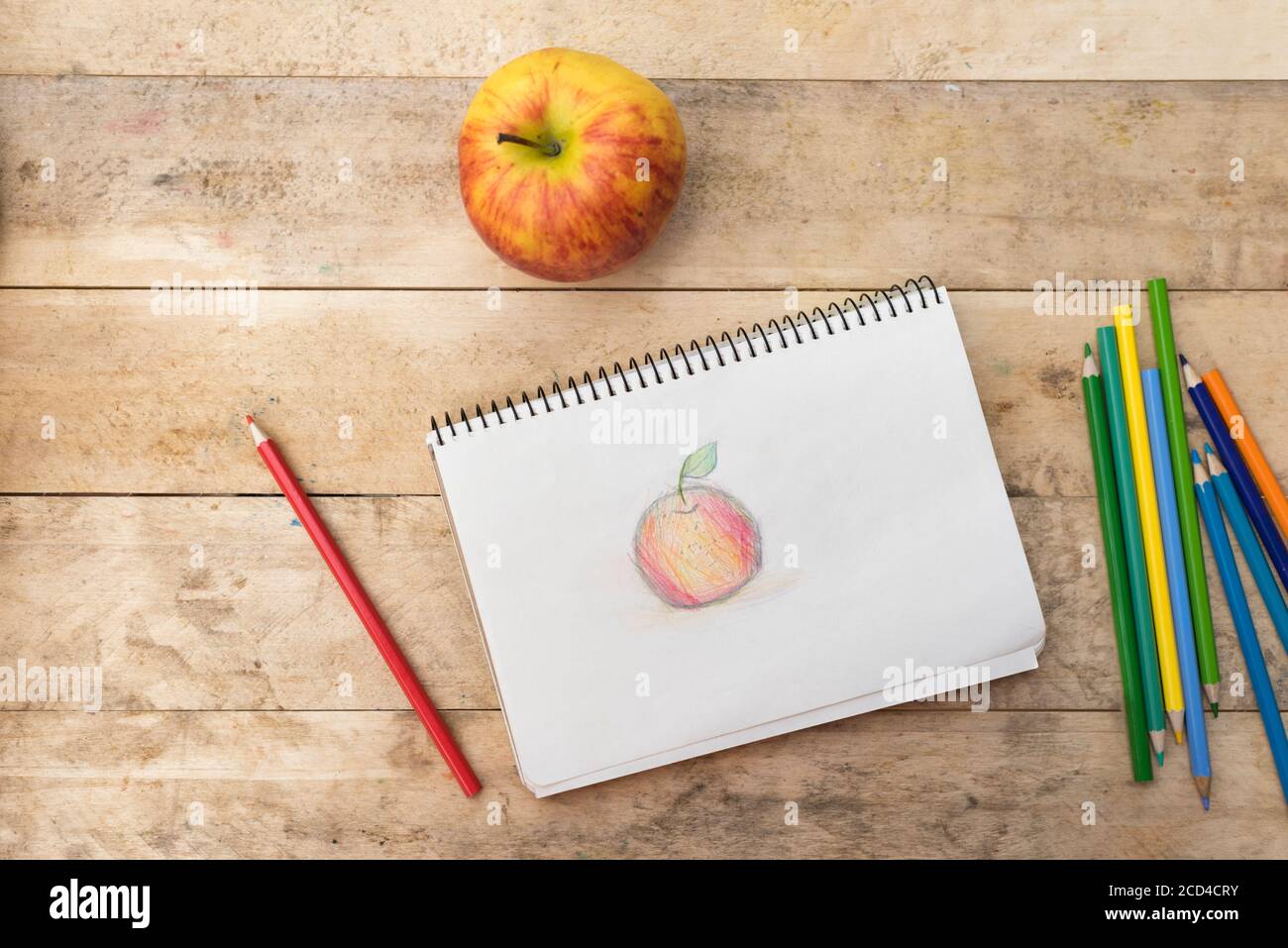 Children's drawing, apple and colored pencils. Wooden table. Top view ...