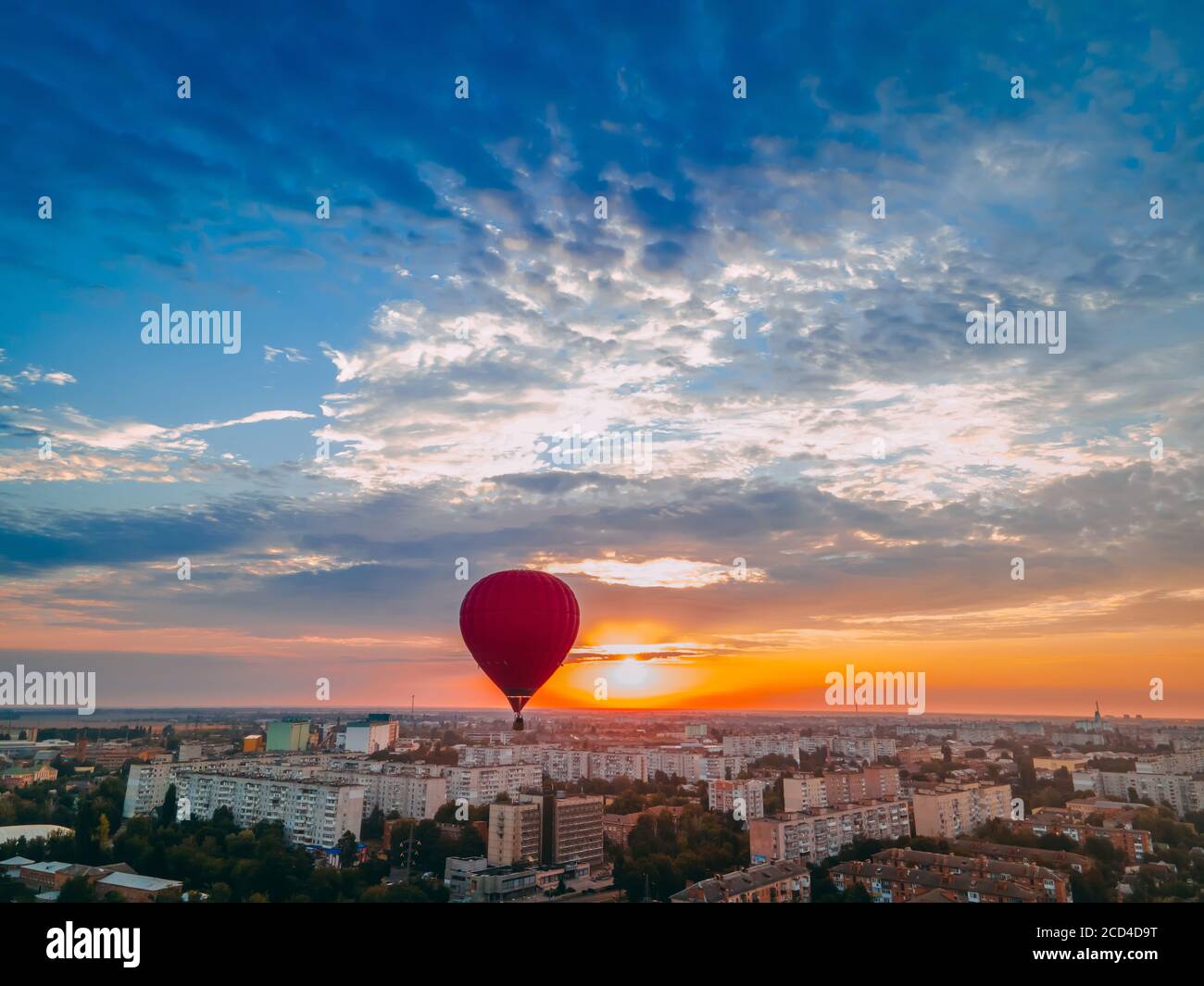 Red hot air balloon flying over small european city at summer sunrise, Kiev region, Ukraine Stock Photo