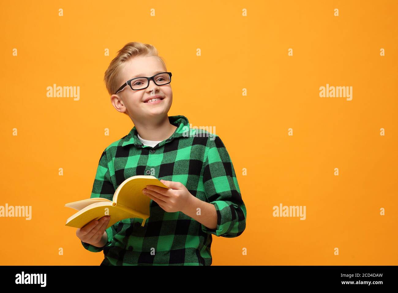 Book reading. Smiling, happy boy reading a book. Portrait of a child on a colored yellow background. Stock Photo