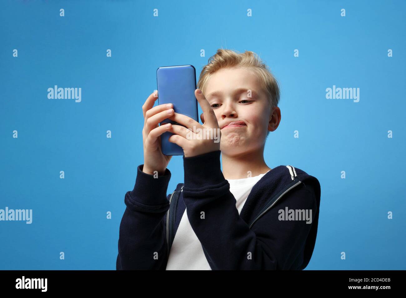 Child talking on a modern smartphone. Smartphone fun. A young boy playing with a smartphone.Portrait of a child on a colored blue background. Emotions Stock Photo