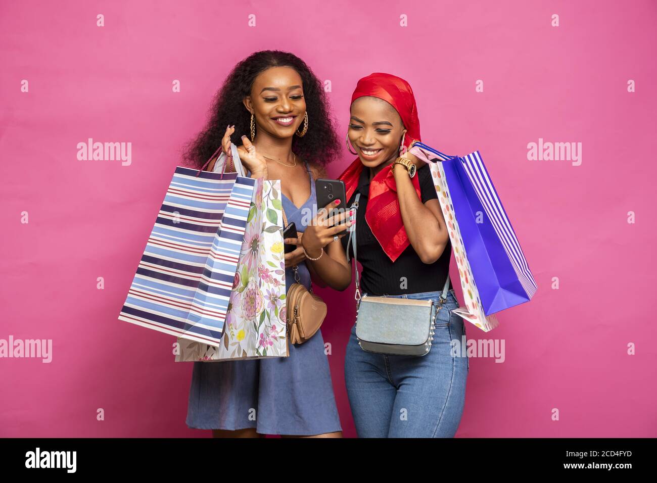 Portrait of two African females holding shopping bags while reacting something in their smartphone Stock Photo