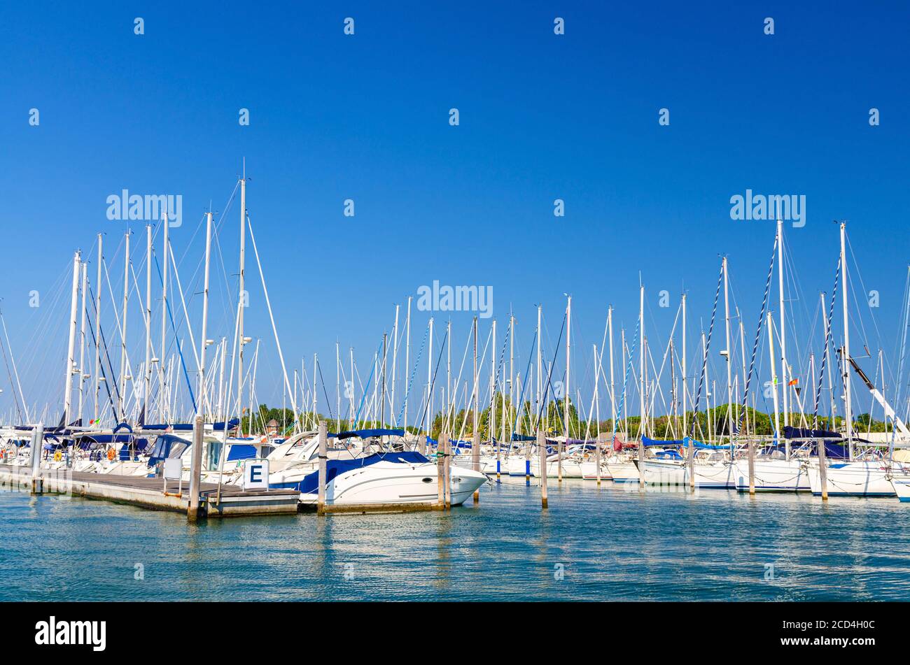 White yachts are moored on water of pier parking in marina port harbour of Sottomarina town in summer day, blue sky background, Veneto Region, Northern Italy Stock Photo