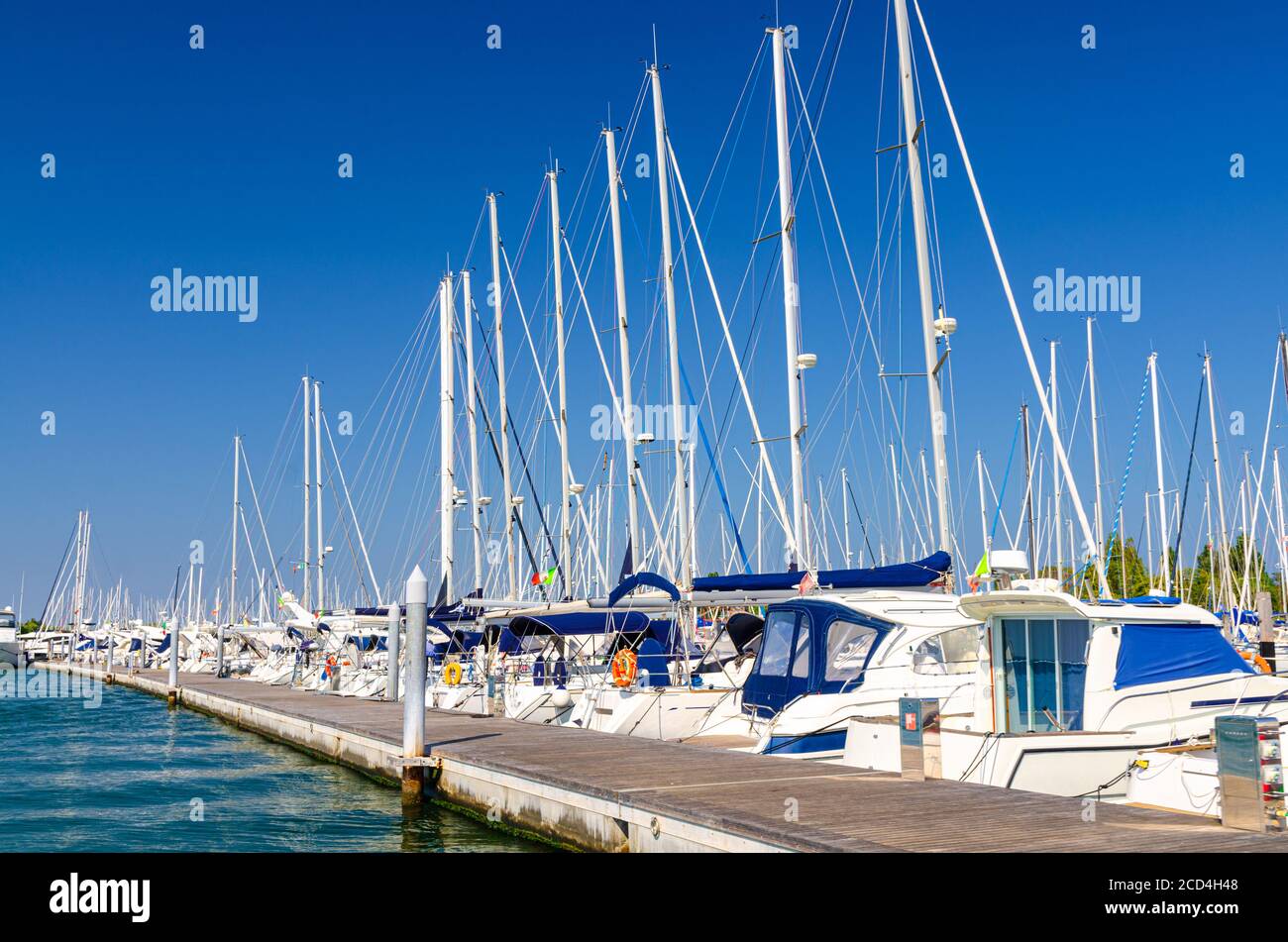 White yachts are moored on water of pier parking in marina port harbour of Sottomarina town in summer day, blue sky background, Veneto Region, Northern Italy Stock Photo